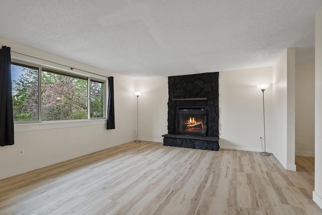 unfurnished living room with a stone fireplace, baseboards, a textured ceiling, and wood finished floors