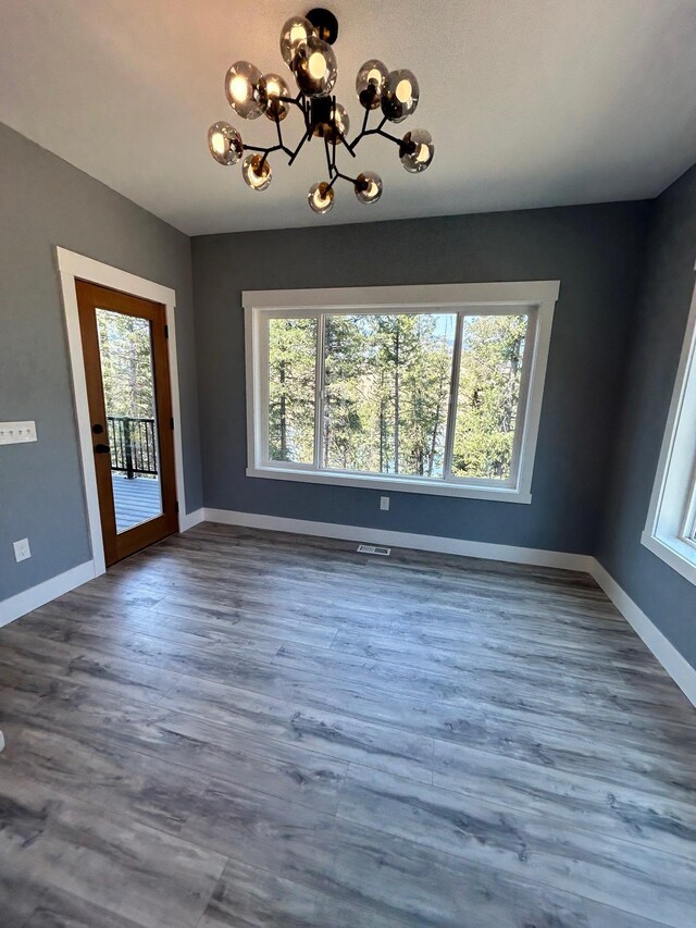 unfurnished dining area featuring a healthy amount of sunlight, baseboards, dark wood-type flooring, and a notable chandelier