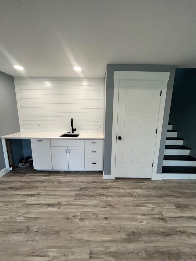 bar featuring wood finished floors, a sink, baseboards, indoor wet bar, and stairs