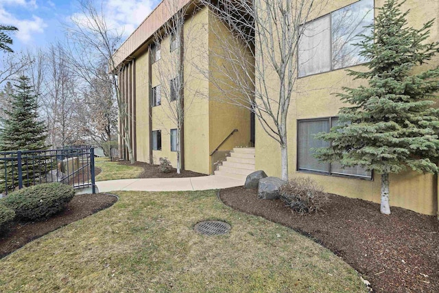 view of side of home with a lawn, stucco siding, and stairs