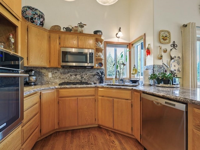 kitchen featuring open shelves, appliances with stainless steel finishes, a sink, decorative backsplash, and wood finished floors