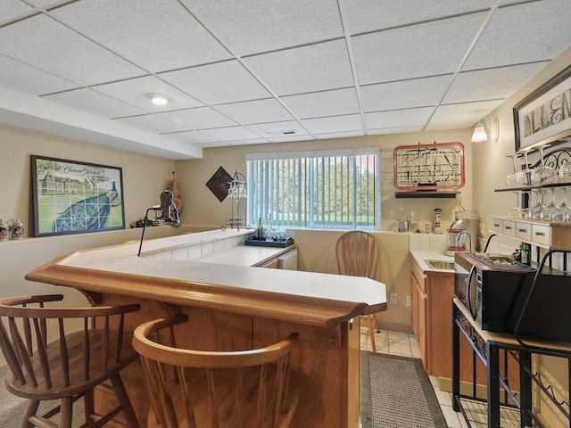 bar with wet bar, a paneled ceiling, black microwave, light tile patterned floors, and a sink
