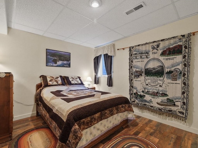 bedroom featuring baseboards, visible vents, a drop ceiling, and wood finished floors