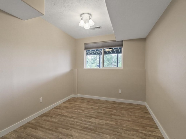 spare room with a textured ceiling, baseboards, visible vents, and wood finished floors