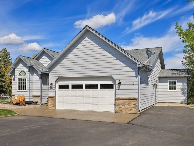 view of front facade with roof with shingles, an attached garage, driveway, and brick siding