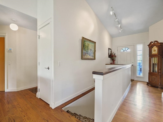 entryway featuring baseboards, vaulted ceiling, light wood finished floors, and rail lighting