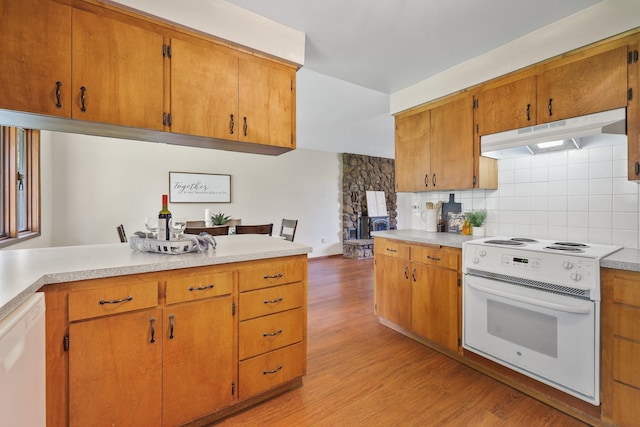 kitchen with light wood-style floors, white appliances, light countertops, backsplash, and under cabinet range hood