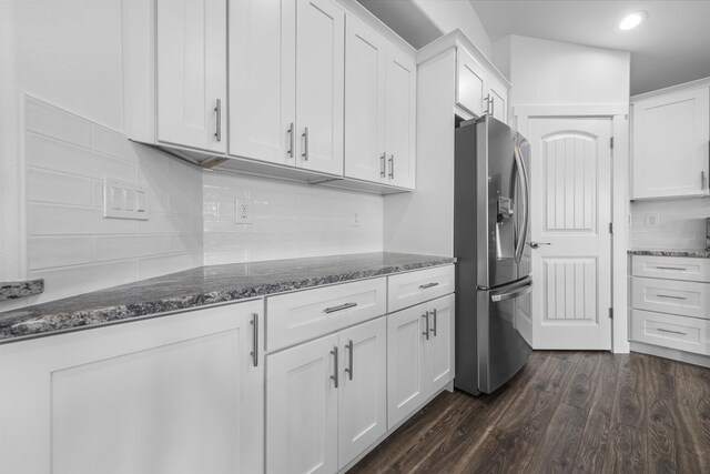 kitchen featuring dark wood-style flooring, tasteful backsplash, white cabinets, dark stone countertops, and stainless steel fridge