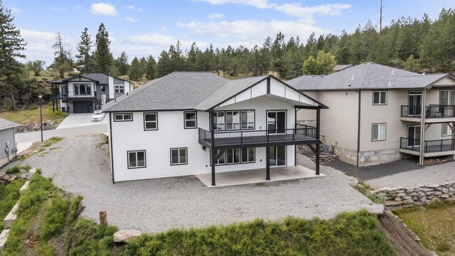 rear view of property with driveway, a shingled roof, a balcony, and a patio area