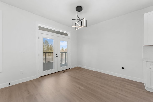 unfurnished dining area with french doors, light wood finished floors, baseboards, and a chandelier