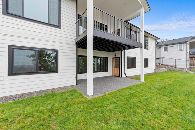 rear view of property featuring a patio, a lawn, fence, and a balcony
