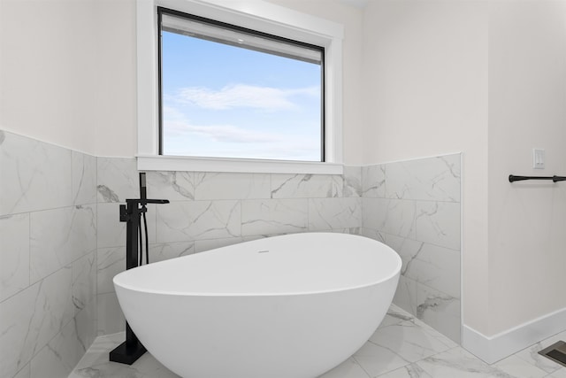bathroom featuring a freestanding tub, tile walls, marble finish floor, and a wainscoted wall