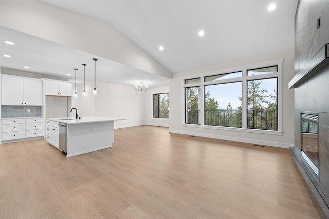 kitchen featuring vaulted ceiling, light countertops, light wood finished floors, open floor plan, and an island with sink
