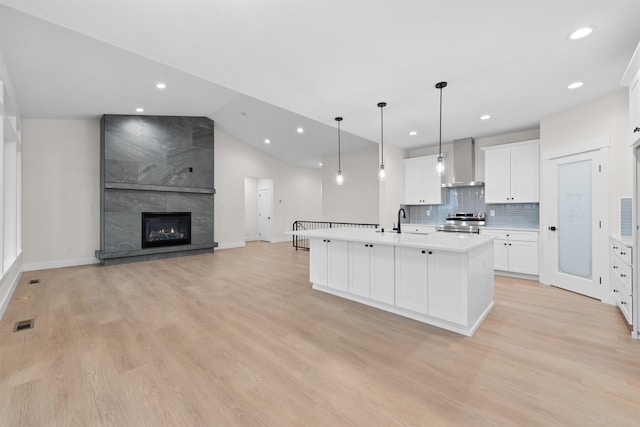 kitchen featuring visible vents, stainless steel range with electric stovetop, wall chimney range hood, and light wood-type flooring