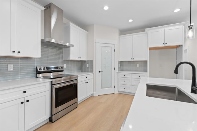 kitchen with stainless steel electric range, white cabinetry, a sink, light wood finished floors, and wall chimney exhaust hood