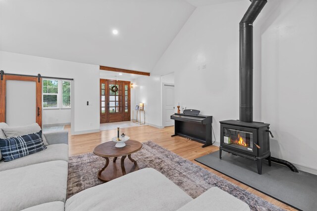 living area featuring baseboards, high vaulted ceiling, light wood finished floors, and a wood stove