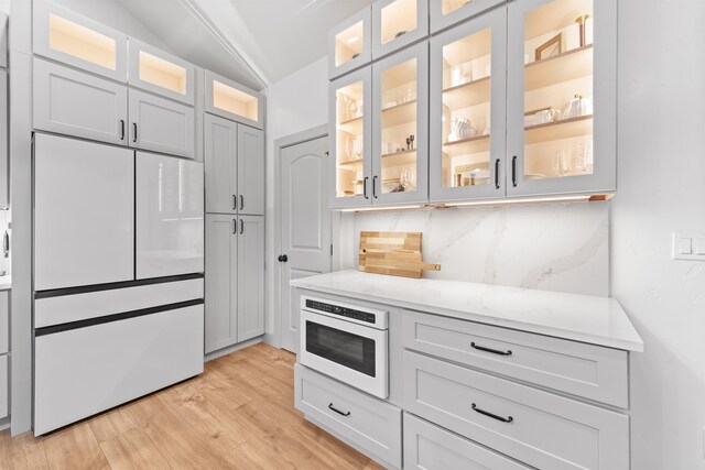 kitchen with glass insert cabinets, decorative backsplash, light wood finished floors, and white appliances