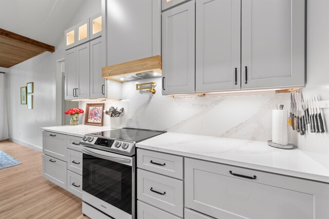 kitchen with glass insert cabinets, light wood-type flooring, light stone counters, electric stove, and backsplash
