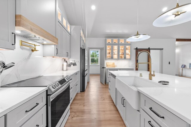 kitchen featuring stainless steel electric range, light stone counters, a sink, light wood-style flooring, and freestanding refrigerator