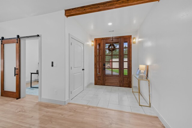 foyer with beam ceiling, baseboards, light wood-style flooring, and a barn door