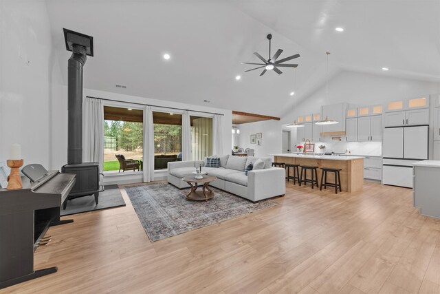 living area with a wood stove, light wood finished floors, a ceiling fan, and high vaulted ceiling