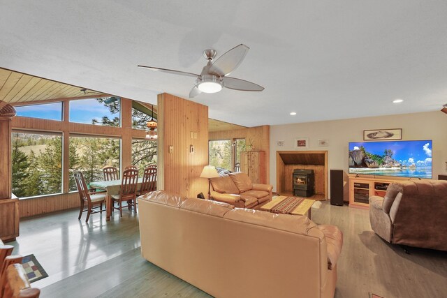 living room featuring a ceiling fan, a wood stove, wood finished floors, lofted ceiling, and wooden walls