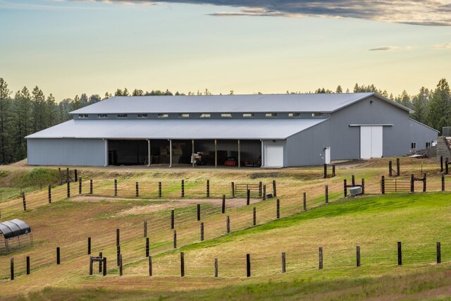 back of property at dusk with an outbuilding, a garage, an exterior structure, a pole building, and a rural view