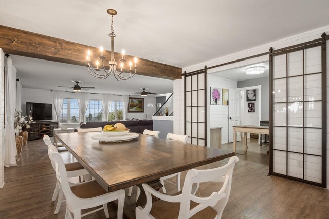 dining area with beamed ceiling, ceiling fan with notable chandelier, dark wood-style flooring, and a barn door