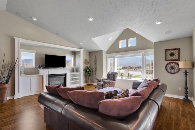 living room featuring a glass covered fireplace, dark wood finished floors, recessed lighting, baseboards, and lofted ceiling