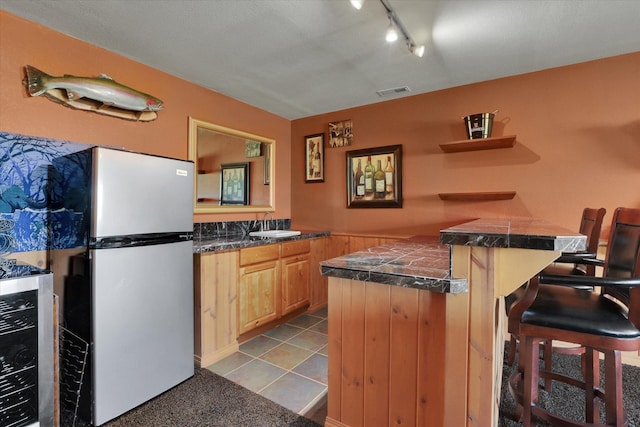 kitchen with open shelves, track lighting, freestanding refrigerator, a peninsula, and a breakfast bar