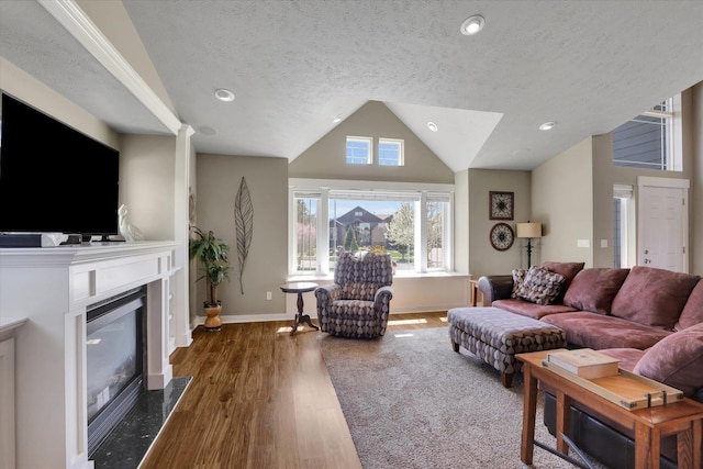 living area featuring a textured ceiling, vaulted ceiling, wood finished floors, baseboards, and a glass covered fireplace