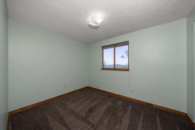 unfurnished room featuring baseboards, dark colored carpet, and a textured ceiling