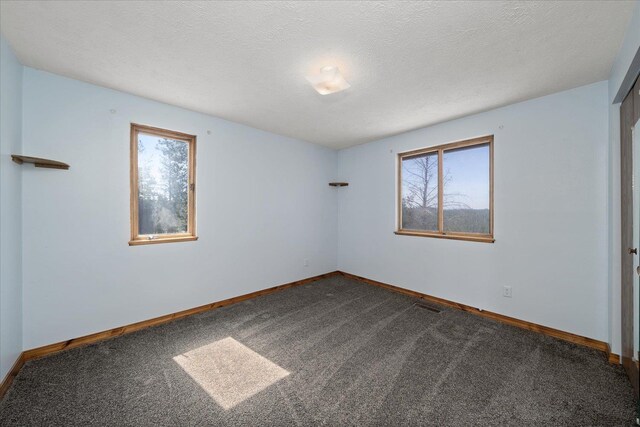 spare room featuring plenty of natural light, baseboards, and dark colored carpet
