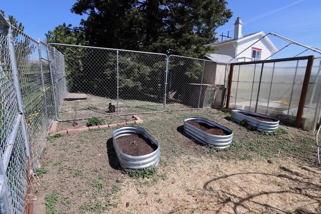 view of yard with fence, a greenhouse, a garden, and an outdoor structure