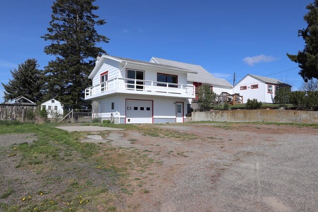exterior space featuring an attached garage, a balcony, and dirt driveway