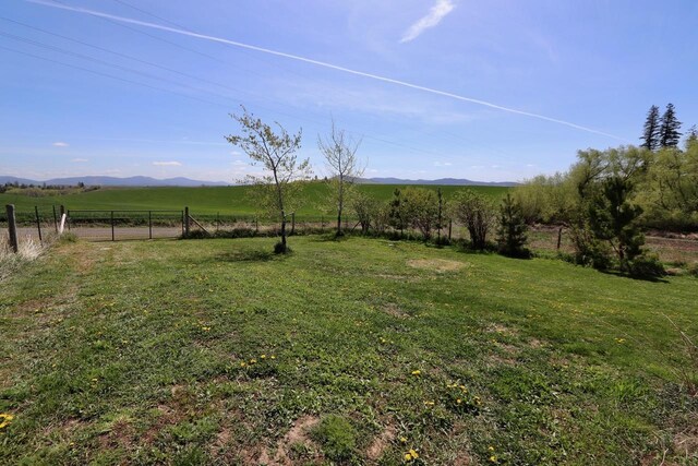 view of yard featuring a rural view, fence, and a mountain view