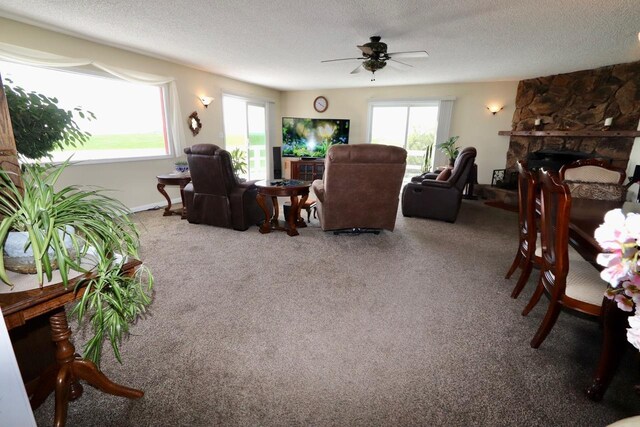 living area with a textured ceiling, ceiling fan, a stone fireplace, and a wealth of natural light