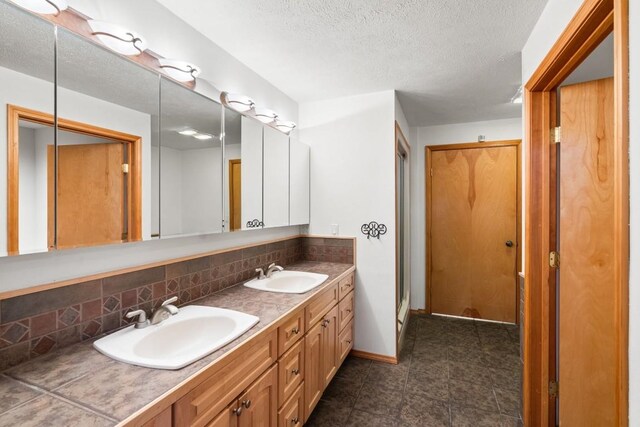 bathroom featuring a sink, a textured ceiling, tasteful backsplash, and double vanity