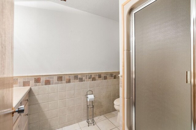 full bathroom featuring vanity, toilet, a wainscoted wall, tile walls, and a shower stall