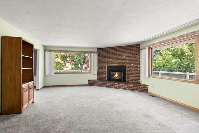 unfurnished living room featuring a brick fireplace, a textured ceiling, baseboards, and carpet