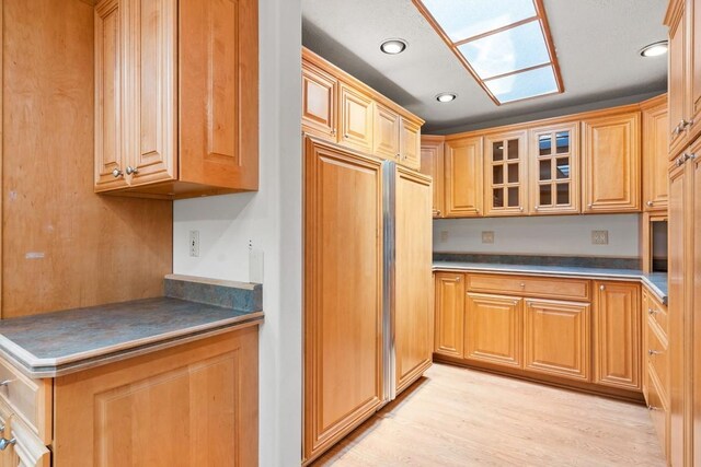 kitchen with glass insert cabinets, dark countertops, recessed lighting, and light wood finished floors