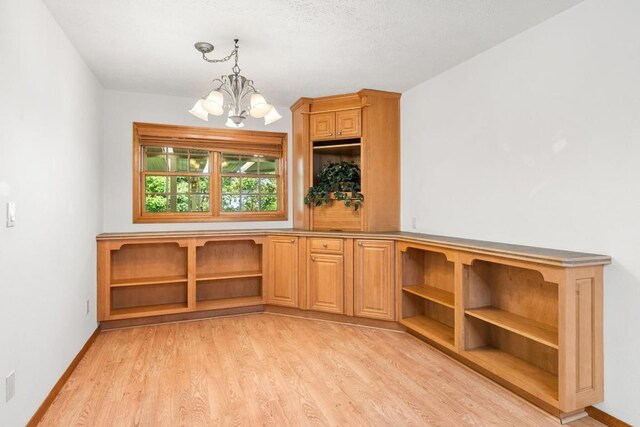 unfurnished dining area featuring baseboards, an inviting chandelier, and light wood finished floors