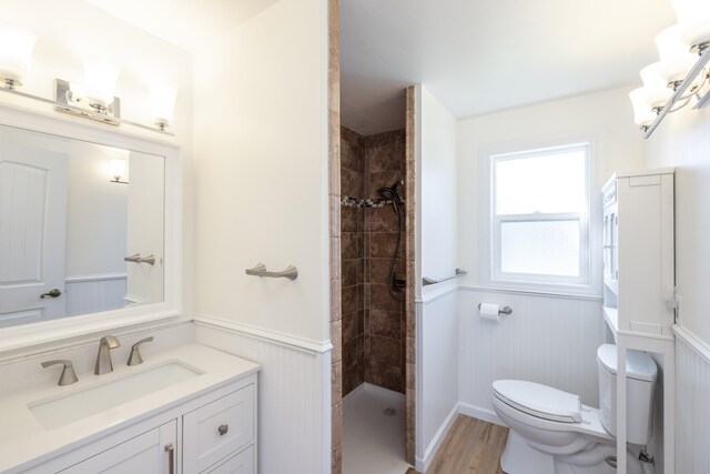 full bathroom with wood finished floors, a wainscoted wall, vanity, toilet, and tiled shower