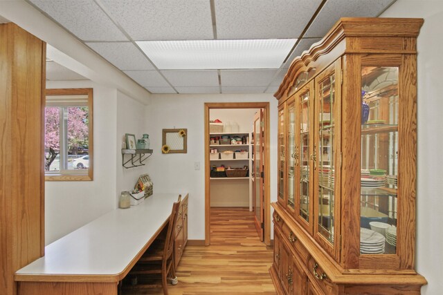 corridor with baseboards, light wood finished floors, and a paneled ceiling