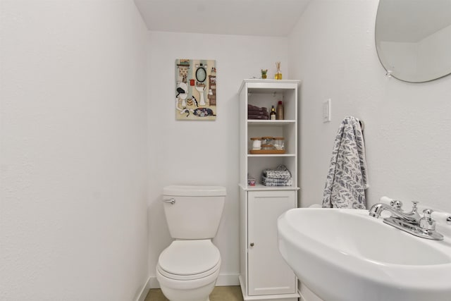 half bathroom with baseboards, a sink, and toilet