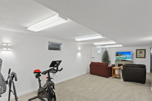 exercise room featuring baseboards, a lit fireplace, and carpet flooring