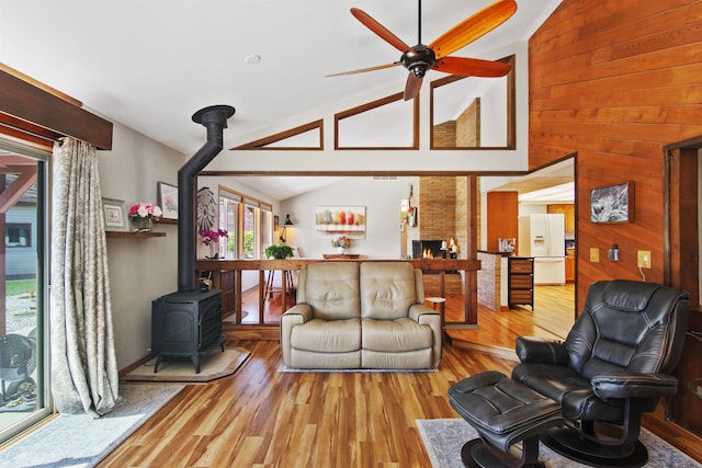 living area featuring a wood stove, wood walls, a ceiling fan, wood finished floors, and lofted ceiling
