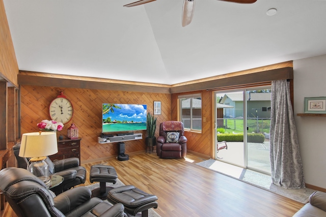 living area featuring a ceiling fan, vaulted ceiling, wood finished floors, baseboards, and wooden walls