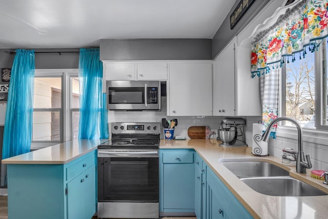 kitchen with a peninsula, a healthy amount of sunlight, blue cabinets, a sink, and stainless steel appliances