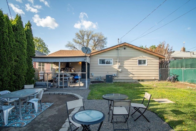 rear view of property featuring fence, a patio, outdoor dining area, central AC unit, and a yard